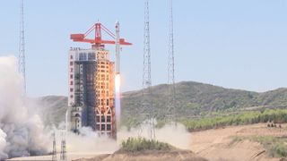 a large white rocket lifts off during the day with mountains visible behind it
