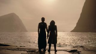 Silhouettes of a man and woman standing side by side, looking off into the sunset over the water.