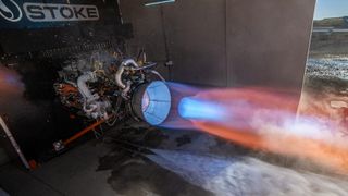 a rocket engine sits horizontally on a test stand outside, belching hot fire